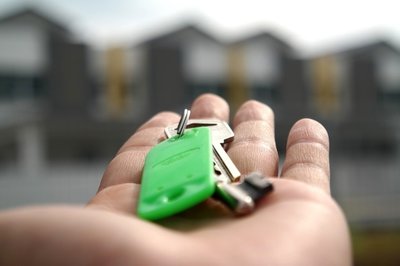 A hand holding out a set of key looking towards an apartment building.